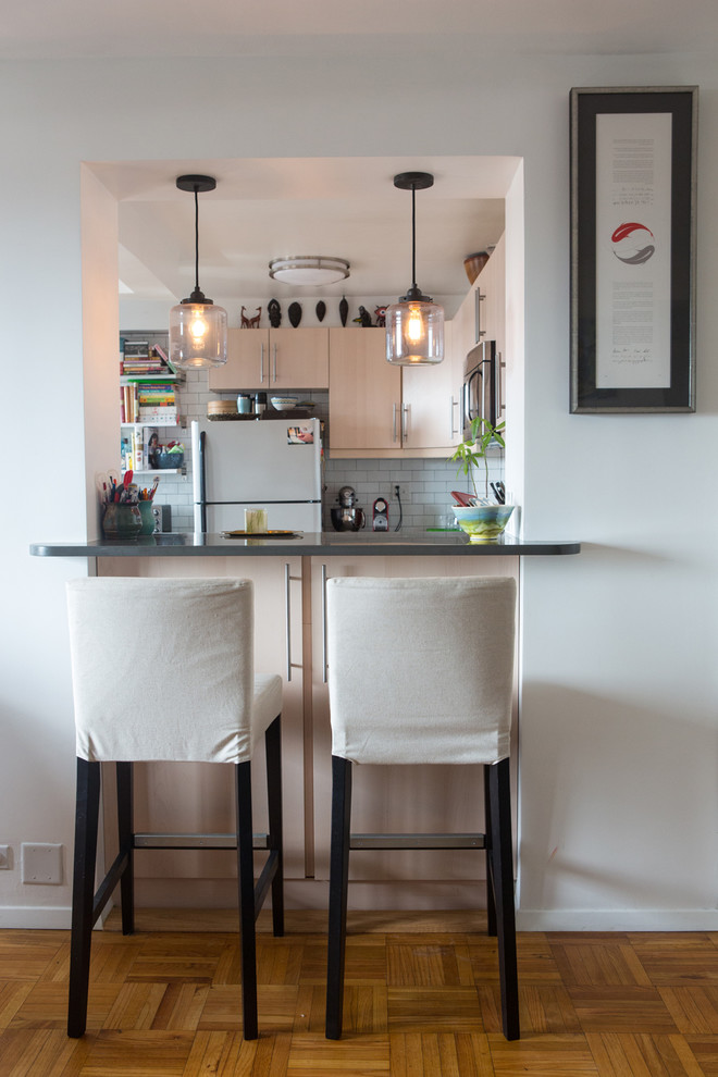 Transitional u-shaped enclosed kitchen photo in New York with flat-panel cabinets, light wood cabinets, white backsplash, subway tile backsplash and white appliances