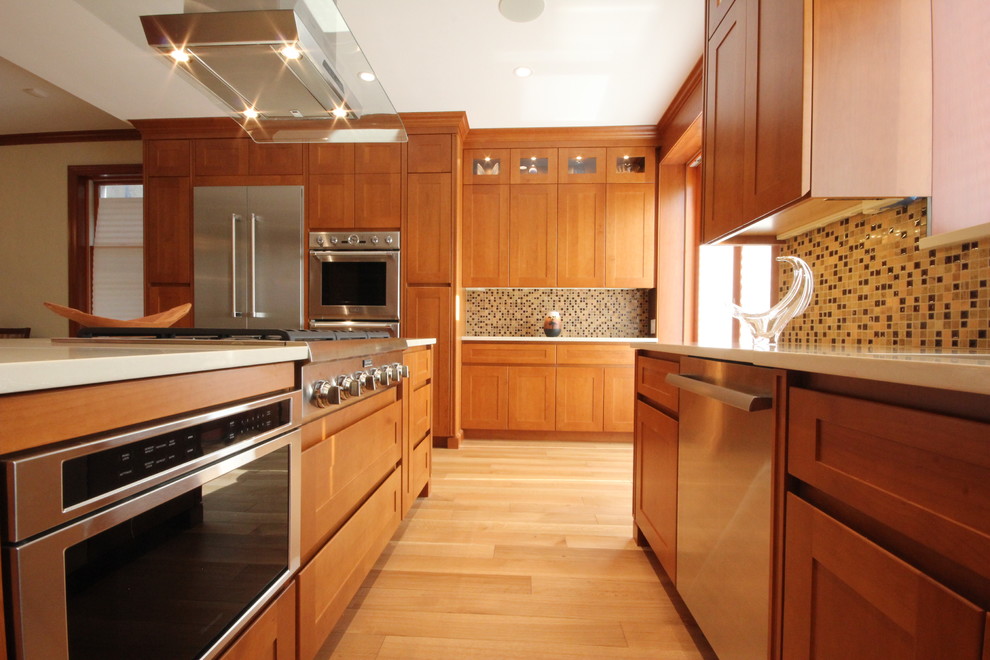 Exempel på ett stort klassiskt kök, med en enkel diskho, skåp i shakerstil, bruna skåp, bänkskiva i kvarts, flerfärgad stänkskydd, stänkskydd i keramik, rostfria vitvaror, ljust trägolv och en köksö