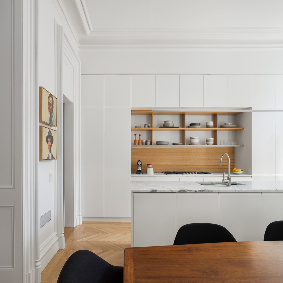 Foto på ett minimalistiskt kök, med en undermonterad diskho, släta luckor, vita skåp, mellanmörkt trägolv och en köksö