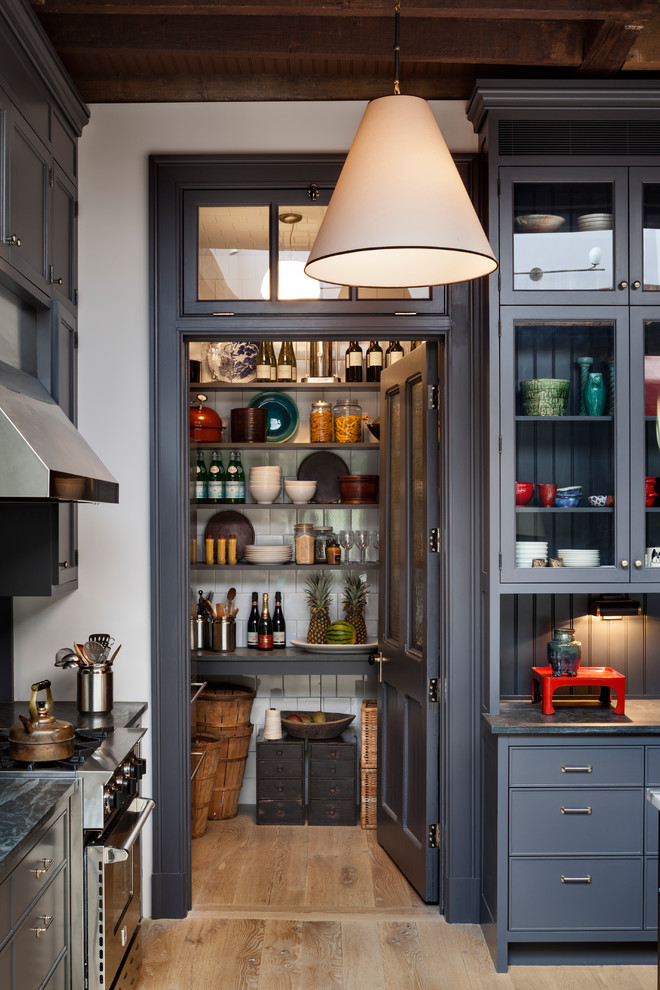 This is an example of a classic u-shaped kitchen pantry in New York with a submerged sink, glass-front cabinets, grey cabinets, marble worktops, grey splashback, wood splashback, stainless steel appliances and light hardwood flooring.
