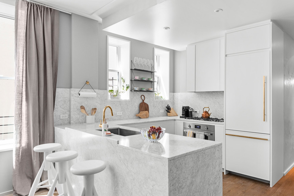 ニューヨークにあるトランジショナルスタイルのおしゃれなキッチン (白いキャビネット、大理石カウンター、大理石のキッチンパネル、アンダーカウンターシンク、フラットパネル扉のキャビネット、白いキッチンパネル、パネルと同色の調理設備、無垢フローリング、茶色い床、白いキッチンカウンター) の写真
