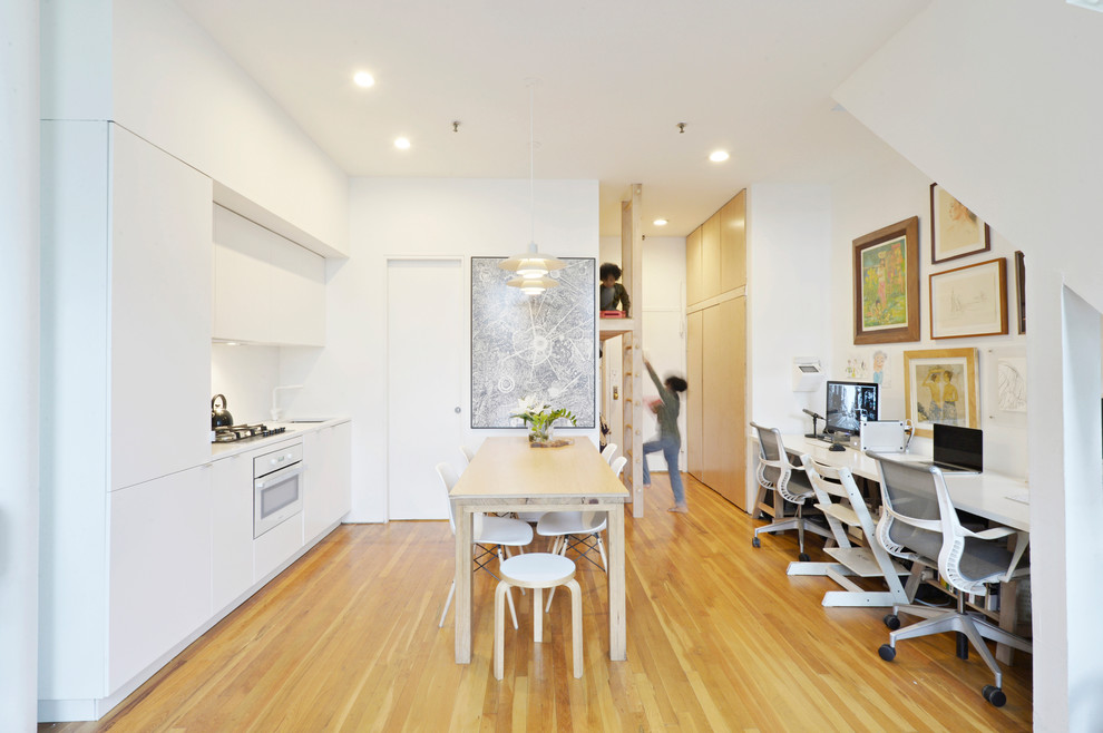 Foto på ett litet funkis linjärt kök och matrum, med en enkel diskho, släta luckor, vita skåp, bänkskiva i kvarts, vitt stänkskydd, integrerade vitvaror, mellanmörkt trägolv och brunt golv