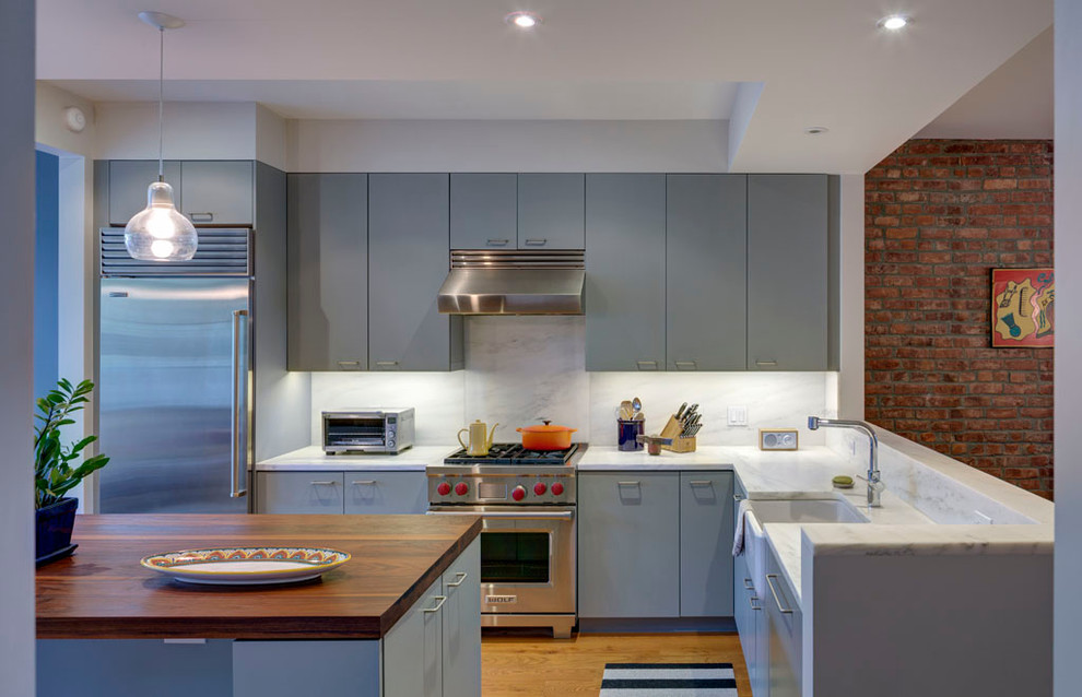 Contemporary l-shaped kitchen in New York with stainless steel appliances, a belfast sink, flat-panel cabinets, grey cabinets, grey splashback, stone slab splashback, marble worktops and light hardwood flooring.