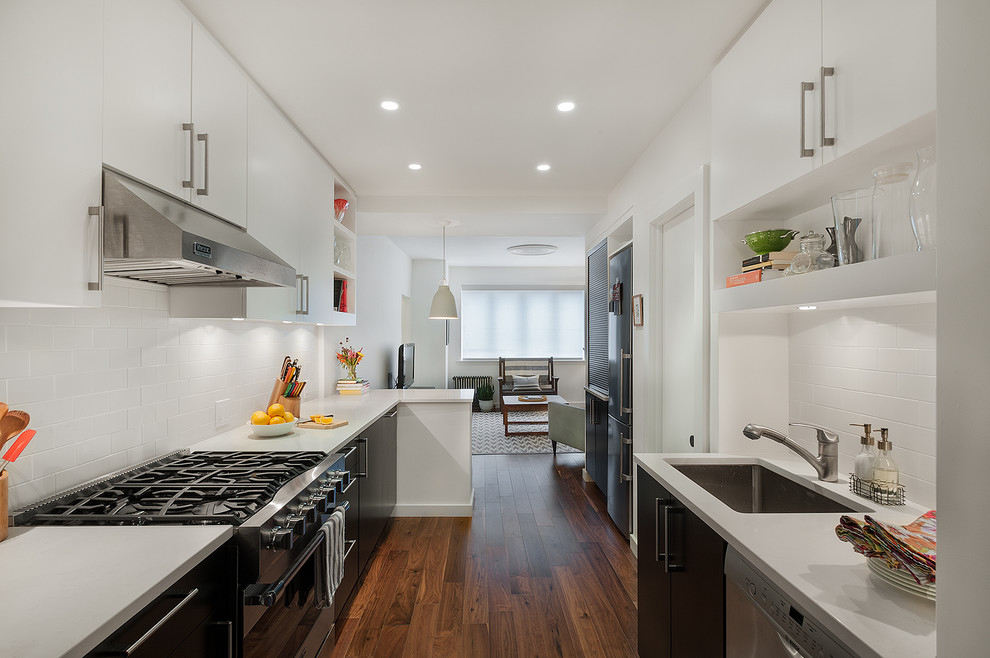 ニューヨークにあるコンテンポラリースタイルのおしゃれなII型キッチン (アンダーカウンターシンク、フラットパネル扉のキャビネット、白いキッチンパネル、サブウェイタイルのキッチンパネル、シルバーの調理設備) の写真