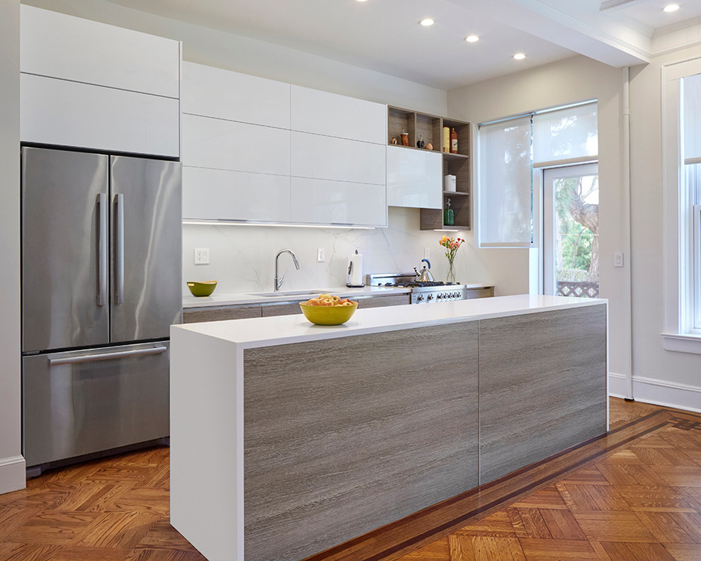 Exempel på ett modernt kök, med en undermonterad diskho, släta luckor, vita skåp, vitt stänkskydd, rostfria vitvaror, mellanmörkt trägolv och en köksö