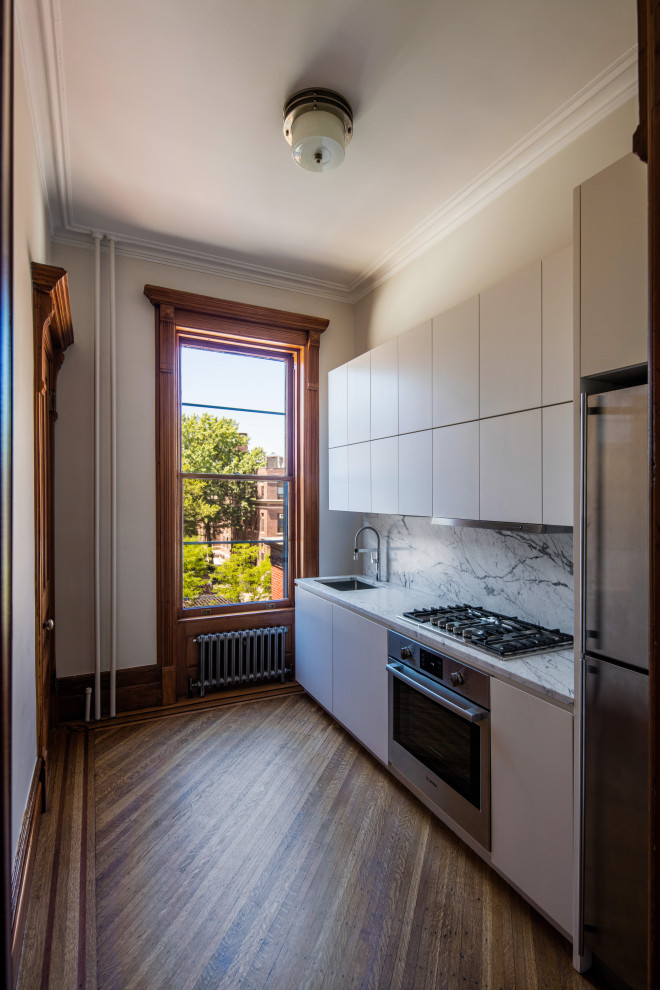 Photo of a small modern single-wall enclosed kitchen in New York with a submerged sink, flat-panel cabinets, white cabinets, marble worktops, grey splashback, marble splashback, stainless steel appliances, medium hardwood flooring, no island, brown floors and grey worktops.