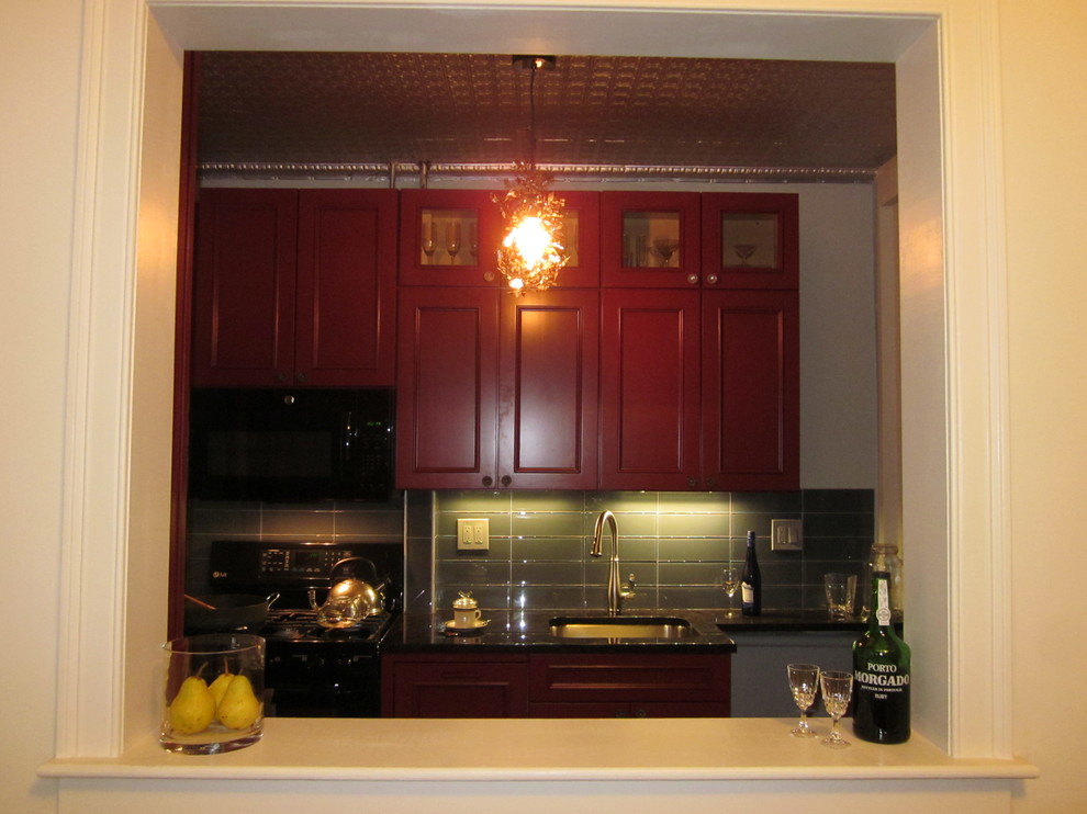 Inredning av ett retro avskilt, litet parallellkök, med en undermonterad diskho, luckor med upphöjd panel, skåp i mellenmörkt trä, grått stänkskydd, stänkskydd i glaskakel, svarta vitvaror, klinkergolv i keramik, en halv köksö och brunt golv