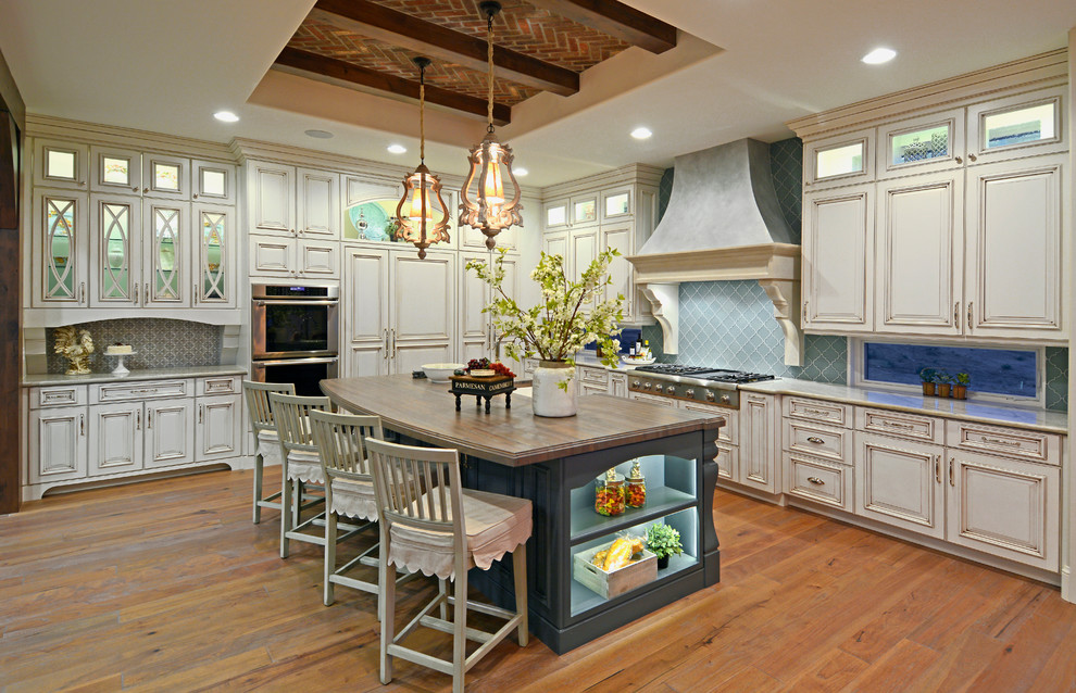 Inspiration for a large transitional l-shaped medium tone wood floor kitchen pantry remodel in Denver with a farmhouse sink, recessed-panel cabinets, white cabinets, granite countertops, blue backsplash, glass tile backsplash, stainless steel appliances and an island