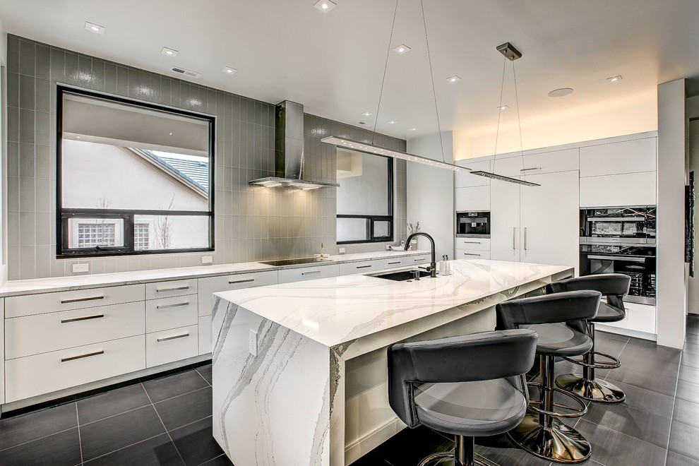 Moderne Küche in grau-weiß mit Unterbauwaschbecken, flächenbündigen Schrankfronten, weißen Schränken, Küchenrückwand in Grau, schwarzen Elektrogeräten, Kücheninsel, schwarzem Boden und weißer Arbeitsplatte in Denver
