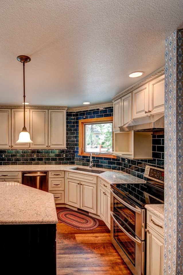 This is an example of a medium sized traditional l-shaped kitchen/diner in Denver with a built-in sink, raised-panel cabinets, white cabinets, engineered stone countertops, blue splashback, ceramic splashback, stainless steel appliances, medium hardwood flooring and an island.