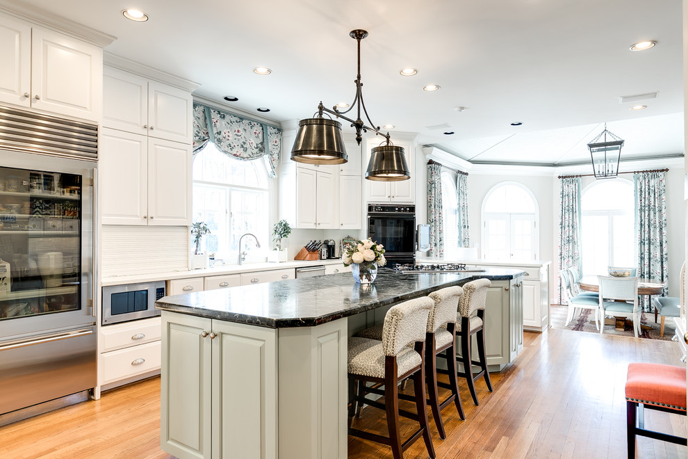Klassische Wohnküche mit profilierten Schrankfronten, weißen Schränken, Küchenrückwand in Weiß, Küchengeräten aus Edelstahl, braunem Holzboden, Kücheninsel und weißer Arbeitsplatte in Richmond