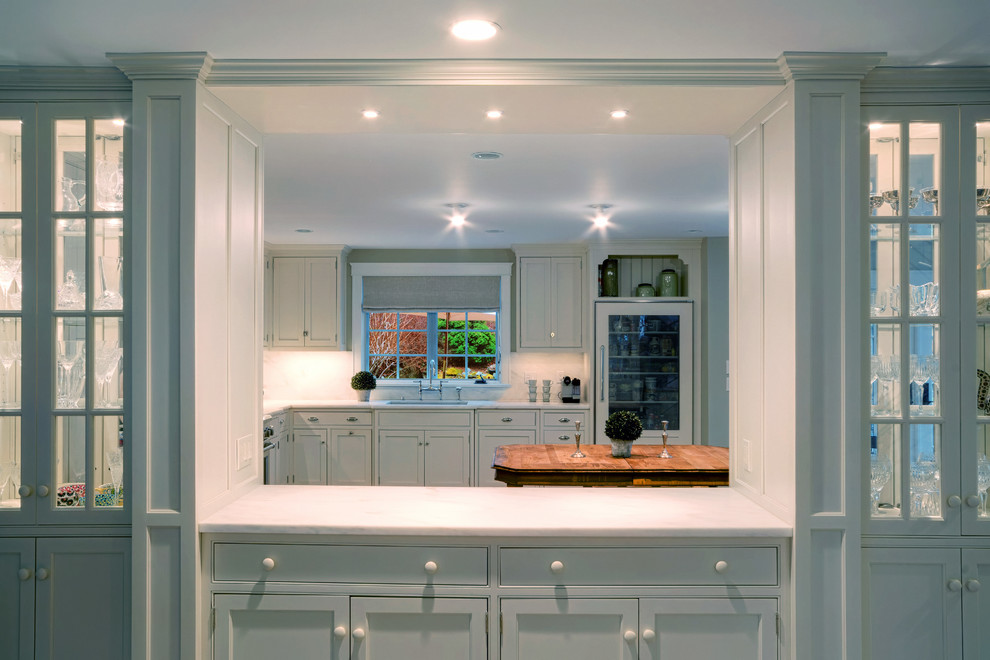 Klassisk inredning av ett stort kök, med en undermonterad diskho, luckor med profilerade fronter, vita skåp, marmorbänkskiva, vitt stänkskydd, stänkskydd i sten, integrerade vitvaror, ljust trägolv och en köksö