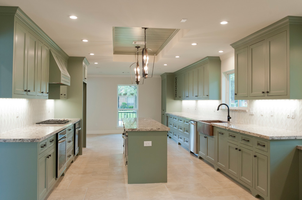 Large island style galley porcelain tile kitchen photo in Houston with a farmhouse sink, recessed-panel cabinets, green cabinets, granite countertops, white backsplash, glass tile backsplash, stainless steel appliances and an island
