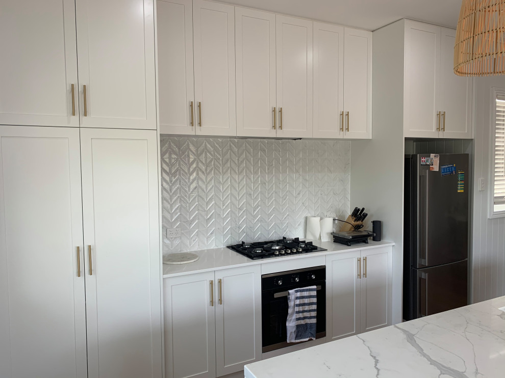 Modern inredning av ett mellanstort vit vitt kök, med skåp i shakerstil, vita skåp, bänkskiva i kvarts, vitt stänkskydd, stänkskydd i keramik, rostfria vitvaror och en köksö