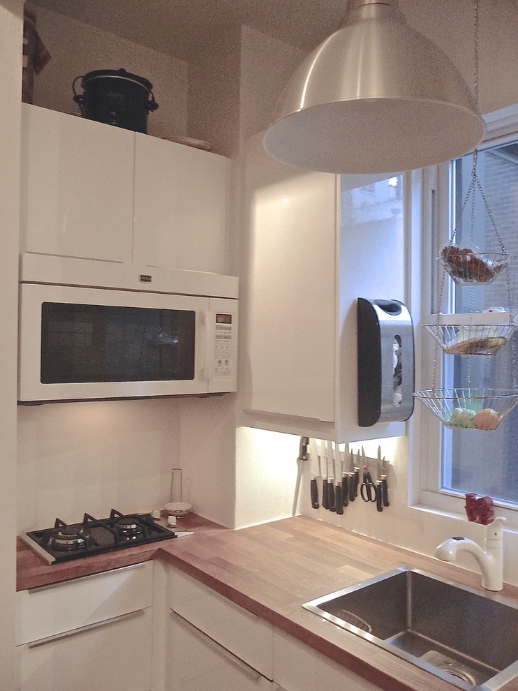 Imagen de cocina lineal contemporánea pequeña cerrada con fregadero encastrado, armarios con paneles lisos, puertas de armario blancas, encimera de madera, electrodomésticos blancos y suelo de madera oscura
