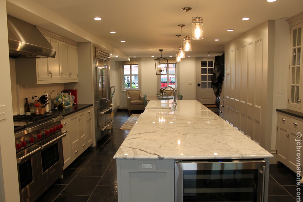 Example of a mid-sized transitional galley limestone floor eat-in kitchen design in New York with a farmhouse sink, shaker cabinets, gray cabinets, marble countertops, white backsplash, subway tile backsplash, stainless steel appliances and an island
