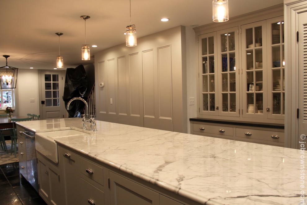 Example of a mid-sized transitional galley limestone floor eat-in kitchen design in New York with a farmhouse sink, shaker cabinets, gray cabinets, marble countertops, white backsplash, subway tile backsplash, stainless steel appliances and an island
