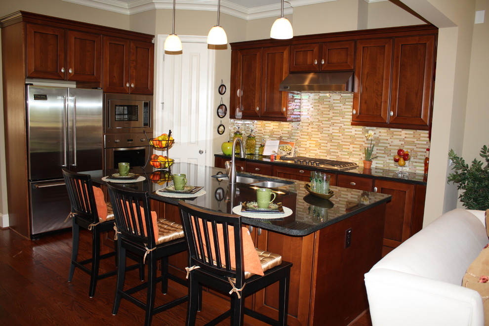 Exempel på ett litet klassiskt kök, med en dubbel diskho, luckor med infälld panel, skåp i mellenmörkt trä, granitbänkskiva, flerfärgad stänkskydd, stänkskydd i glaskakel, rostfria vitvaror, mellanmörkt trägolv och en köksö