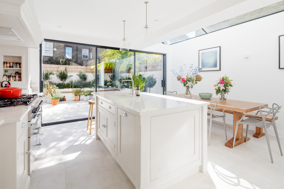 Mid-sized elegant galley porcelain tile and beige floor eat-in kitchen photo in London with a drop-in sink, shaker cabinets, white cabinets, solid surface countertops, white backsplash, ceramic backsplash, stainless steel appliances and an island