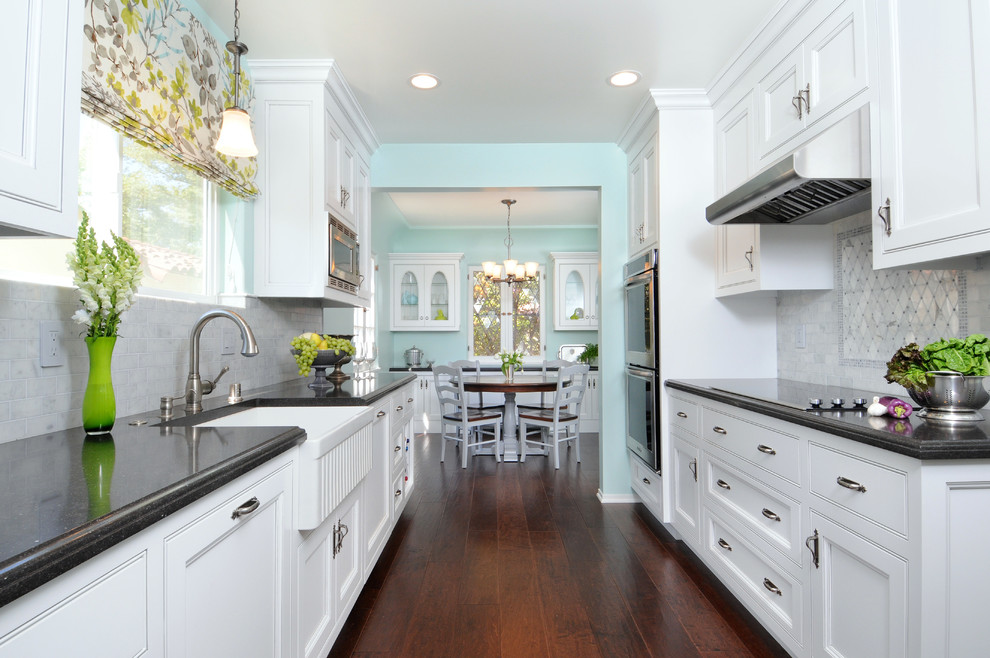 Example of a classic galley eat-in kitchen design in Los Angeles with a farmhouse sink, beaded inset cabinets, white cabinets, white backsplash, stainless steel appliances and stone tile backsplash