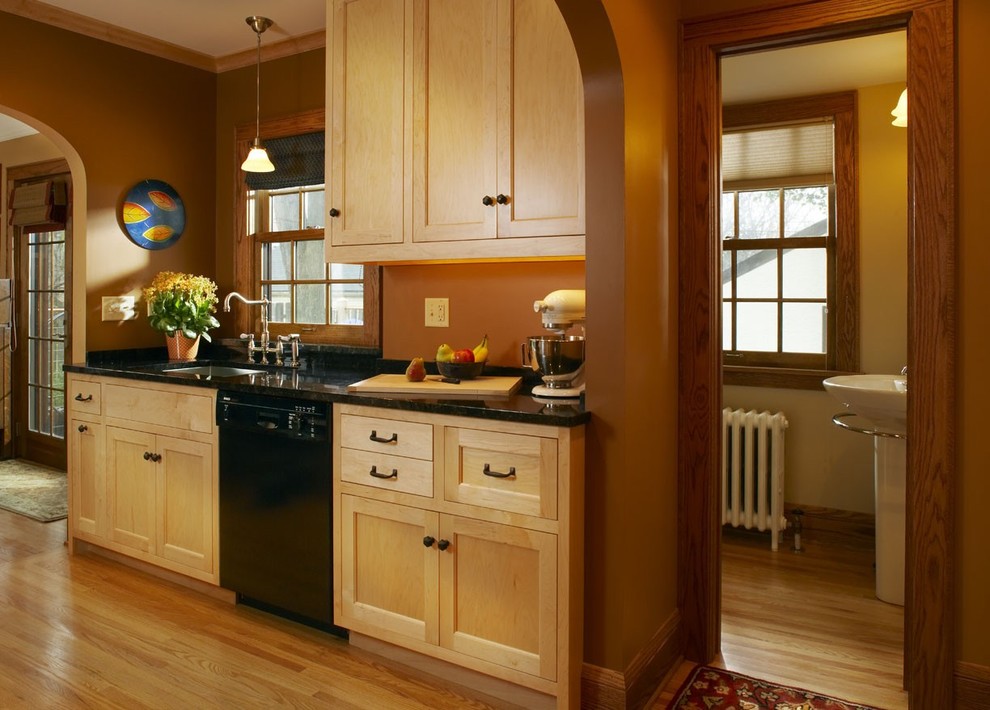 На фото: кухня в классическом стиле с фасадами с утопленной филенкой, светлыми деревянными фасадами, черной техникой и мойкой у окна