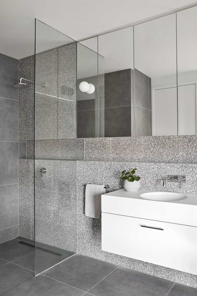 Foto på ett funkis vit badrum med dusch, med släta luckor, vita skåp, en kantlös dusch, grå kakel, ett integrerad handfat, grått golv och med dusch som är öppen