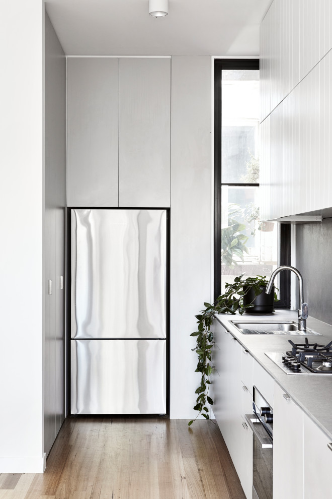 Inredning av ett modernt mellanstort grå grått l-kök, med en undermonterad diskho, släta luckor, vita skåp, grått stänkskydd, rostfria vitvaror och beiget golv