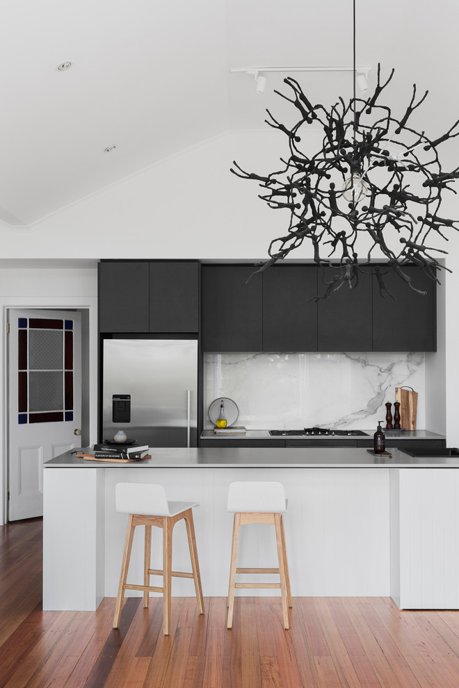 Inredning av ett modernt kök, med en integrerad diskho, släta luckor, svarta skåp, bänkskiva i betong, vitt stänkskydd, stänkskydd i marmor, rostfria vitvaror, mellanmörkt trägolv, en halv köksö och brunt golv