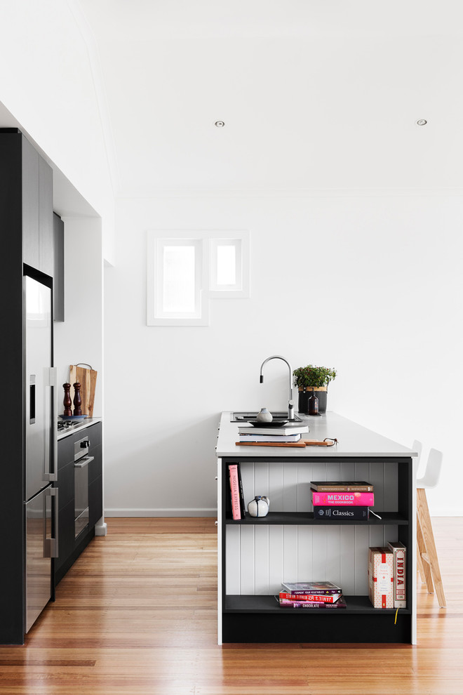Inredning av ett modernt kök, med en integrerad diskho, släta luckor, svarta skåp, bänkskiva i betong, vitt stänkskydd, stänkskydd i marmor, rostfria vitvaror, mellanmörkt trägolv och en halv köksö