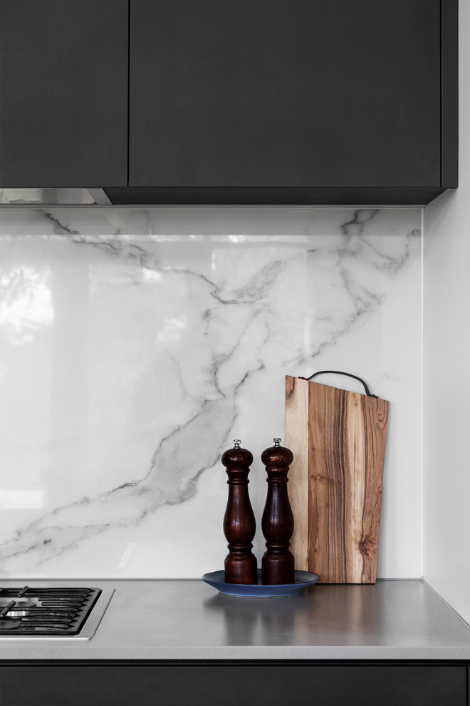 Modern inredning av ett kök, med en integrerad diskho, släta luckor, svarta skåp, bänkskiva i betong, vitt stänkskydd, stänkskydd i marmor, rostfria vitvaror, mellanmörkt trägolv och en halv köksö