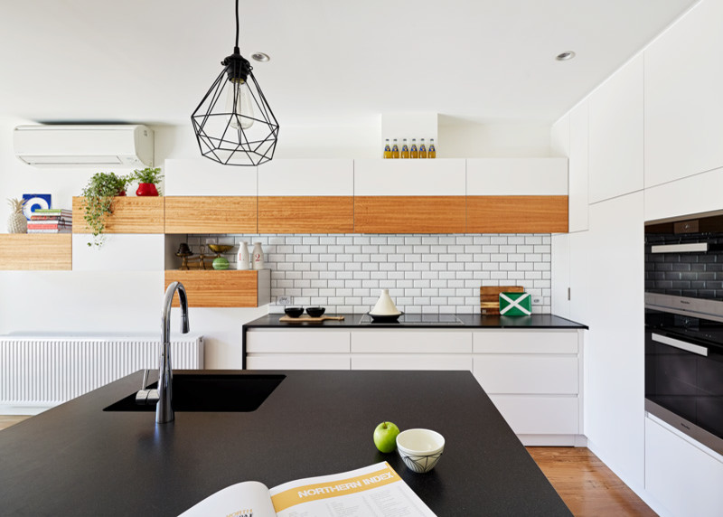 Modelo de cocina actual de tamaño medio con salpicadero blanco, salpicadero de azulejos tipo metro, electrodomésticos de acero inoxidable y una isla