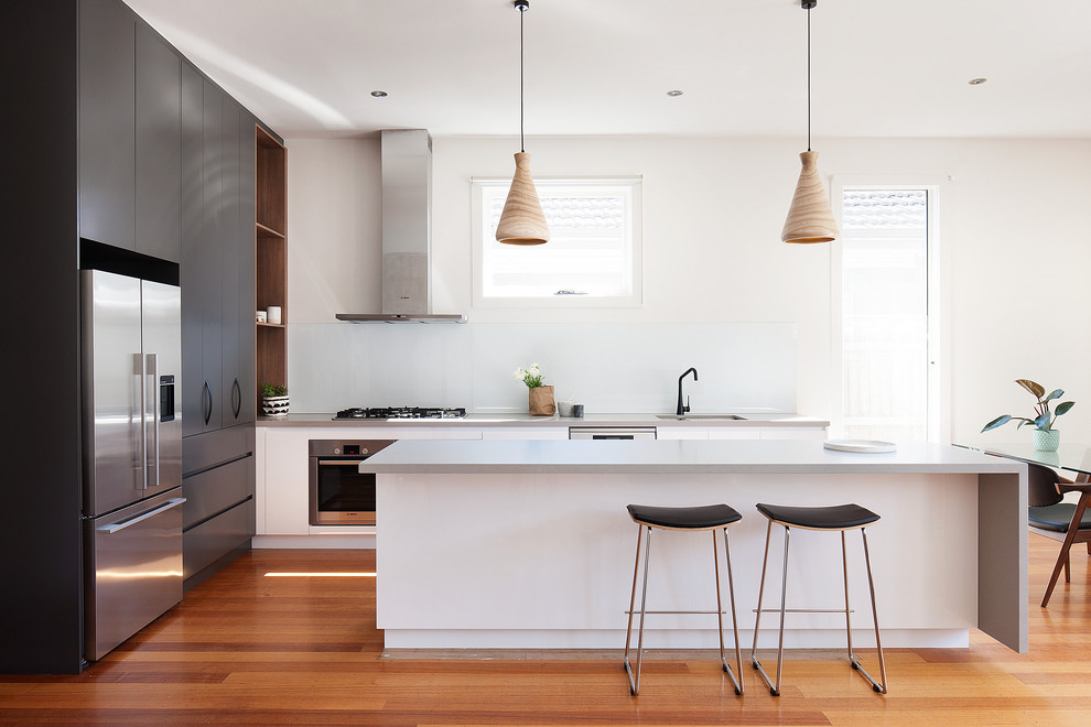 Immagine di una grande cucina minimal con lavello sottopiano, ante lisce, ante nere, paraspruzzi bianco, elettrodomestici in acciaio inossidabile e pavimento in legno massello medio