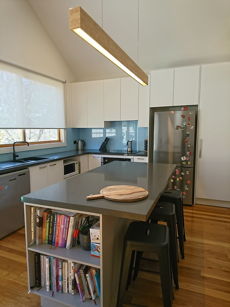 Photo of a small modern l-shaped open plan kitchen in Melbourne with a built-in sink, flat-panel cabinets, grey cabinets, engineered stone countertops, blue splashback, glass sheet splashback, medium hardwood flooring, an island and grey worktops.