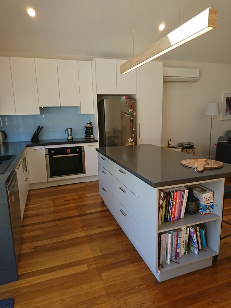 Inspiration for a small modern l-shaped open plan kitchen in Melbourne with a built-in sink, flat-panel cabinets, grey cabinets, engineered stone countertops, blue splashback, glass sheet splashback, medium hardwood flooring, an island and grey worktops.