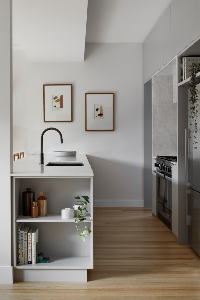 Photo of a small modern l-shaped kitchen in Melbourne with a built-in sink, grey cabinets, marble worktops, grey splashback, marble splashback, stainless steel appliances, light hardwood flooring and white worktops.