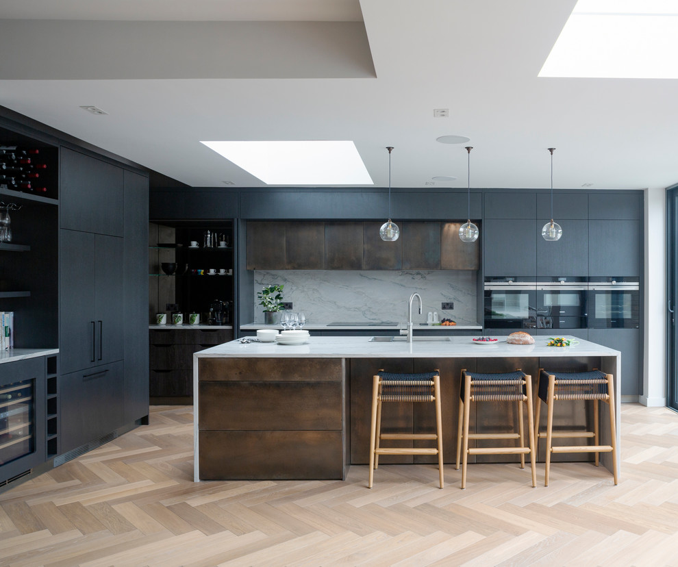 Example of a trendy light wood floor and beige floor kitchen design in London with flat-panel cabinets, black cabinets, quartzite countertops, white backsplash, stone slab backsplash, black appliances, an island, white countertops and an undermount sink