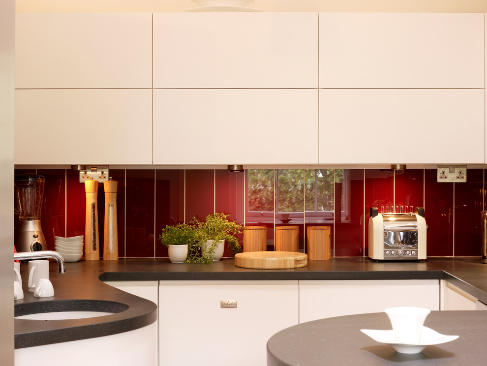 Medium sized contemporary u-shaped open plan kitchen in London with a built-in sink, flat-panel cabinets, white cabinets, wood worktops, red splashback, integrated appliances, medium hardwood flooring and a breakfast bar.