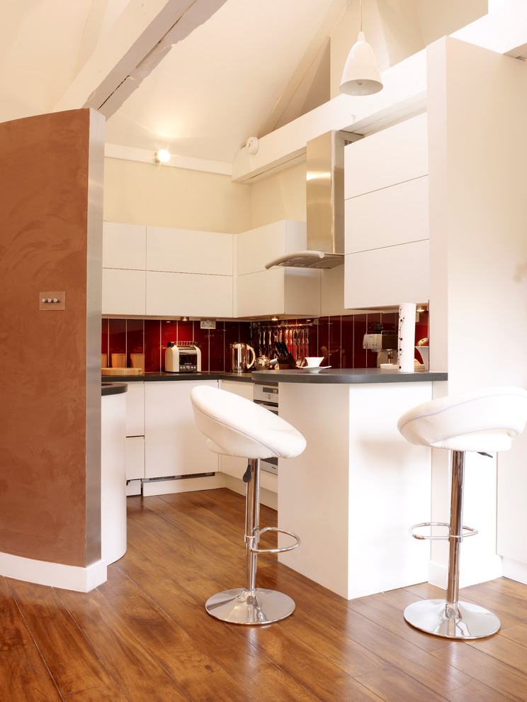 ロンドンにある中くらいなコンテンポラリースタイルのおしゃれなキッチン (フラットパネル扉のキャビネット、白いキャビネット、赤いキッチンパネル、無垢フローリング、ドロップインシンク、木材カウンター、パネルと同色の調理設備) の写真
