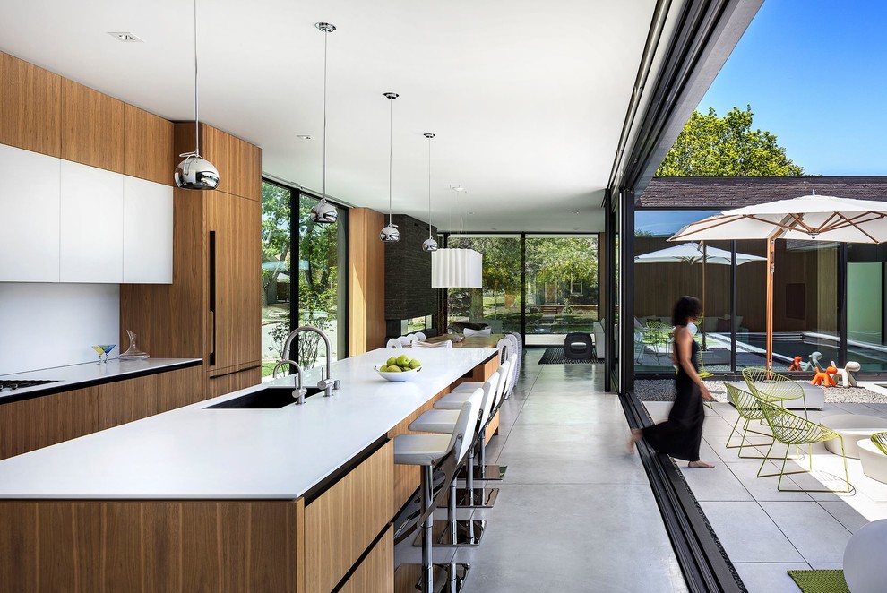 Идея дизайна: кухня-гостиная в современном стиле с врезной мойкой, плоскими фасадами, фасадами цвета дерева среднего тона, техникой под мебельный фасад, бетонным полом, островом и серым полом