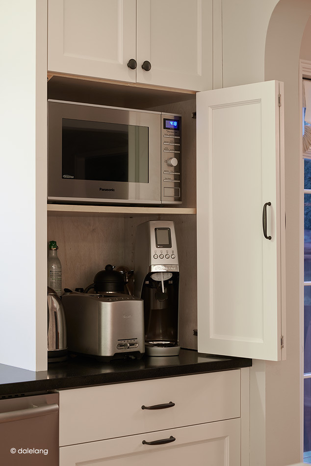 Exempel på ett lantligt kök, med en rustik diskho, luckor med profilerade fronter, vita skåp, vitt stänkskydd, stänkskydd i stenkakel, rostfria vitvaror, ljust trägolv och en köksö
