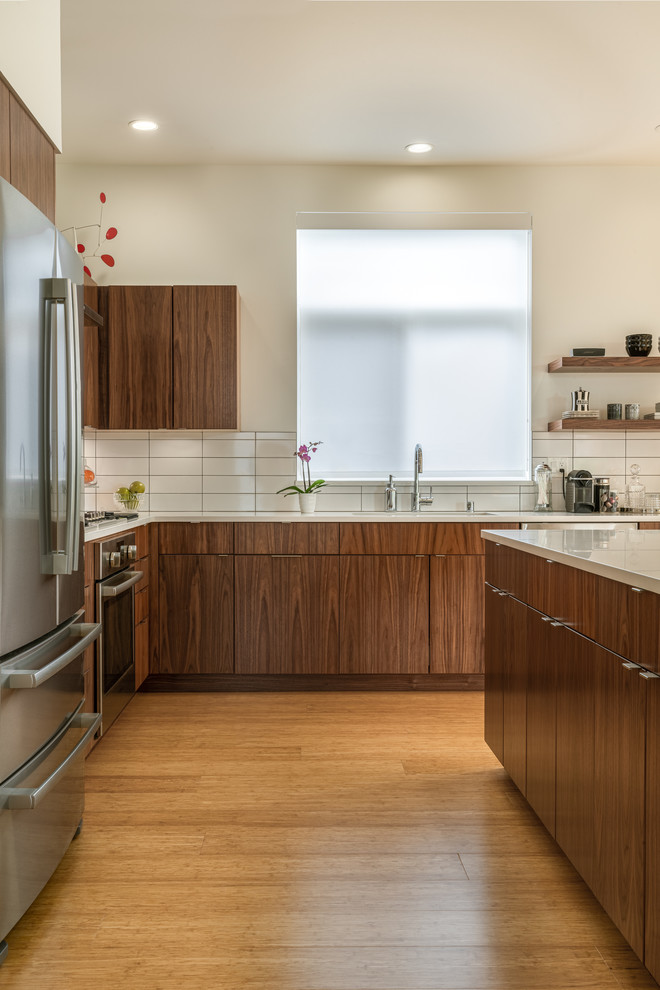 Idéer för ett mellanstort modernt vit kök, med en undermonterad diskho, släta luckor, skåp i mellenmörkt trä, bänkskiva i kvarts, vitt stänkskydd, stänkskydd i porslinskakel, rostfria vitvaror, bambugolv, en köksö och brunt golv