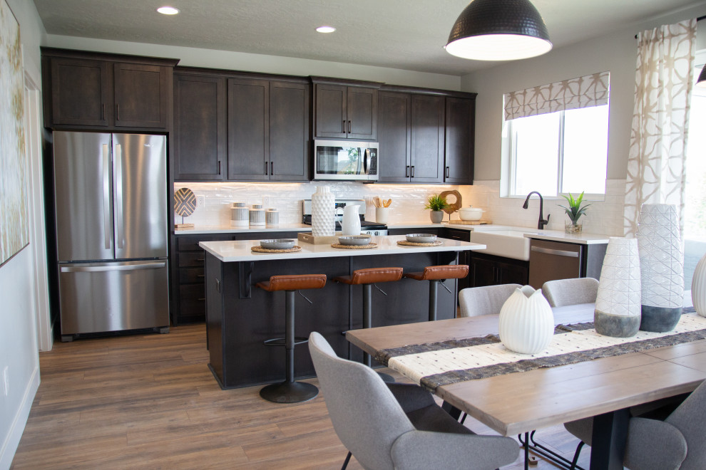 Transitional l-shaped medium tone wood floor and brown floor kitchen photo in Salt Lake City with a farmhouse sink, shaker cabinets, dark wood cabinets, stainless steel appliances, an island and white countertops