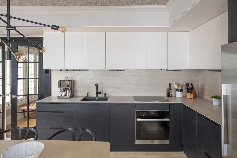 Cette image montre une cuisine design en L avec un évier 1 bac, un placard à porte plane, des portes de placard blanches, une crédence beige et un électroménager en acier inoxydable.