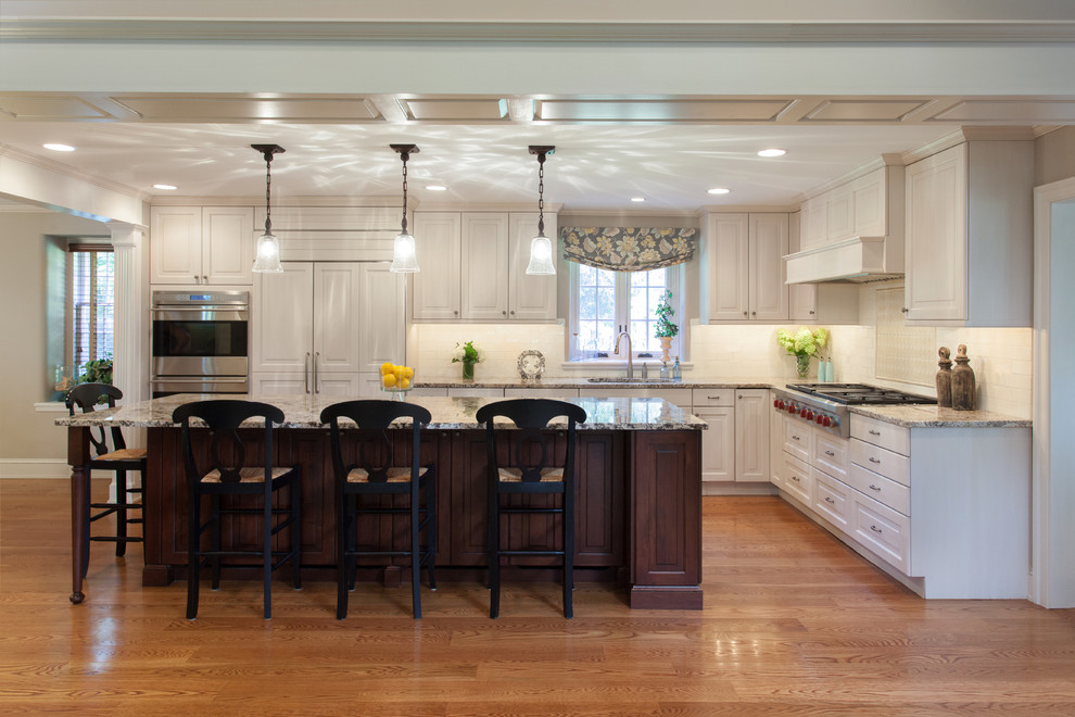 Foto på ett lantligt kök, med luckor med upphöjd panel, vita skåp, granitbänkskiva, vitt stänkskydd, stänkskydd i porslinskakel, rostfria vitvaror och mellanmörkt trägolv