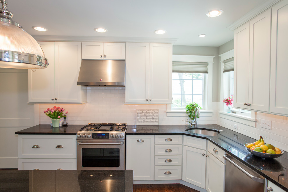 Example of a mid-sized classic l-shaped dark wood floor eat-in kitchen design in Philadelphia with an undermount sink, flat-panel cabinets, white cabinets, granite countertops, white backsplash, subway tile backsplash, stainless steel appliances and an island