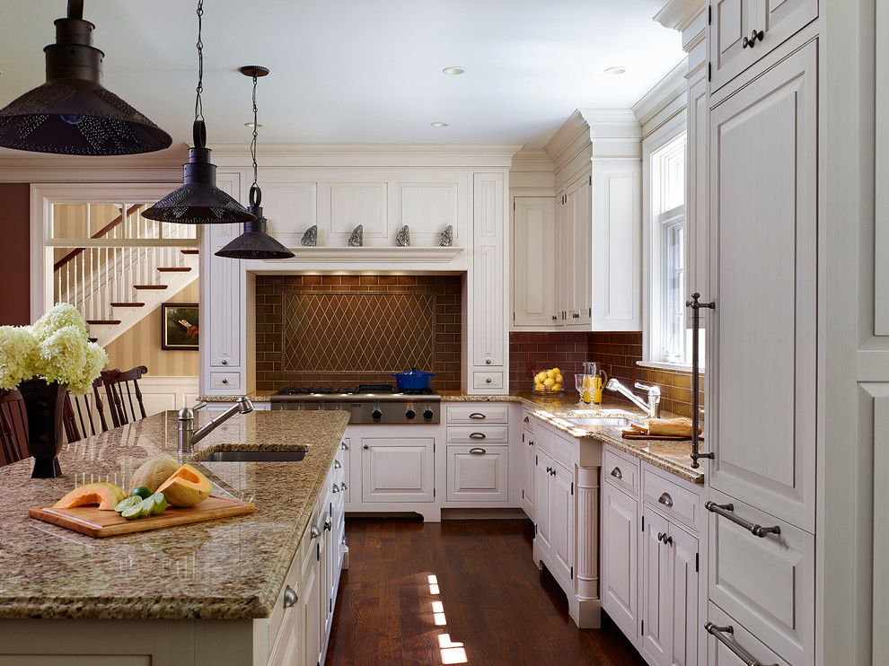 Inspiration for a large timeless l-shaped medium tone wood floor and brown floor kitchen remodel in Philadelphia with an undermount sink, raised-panel cabinets, white cabinets, brown backsplash, subway tile backsplash, paneled appliances, granite countertops and an island