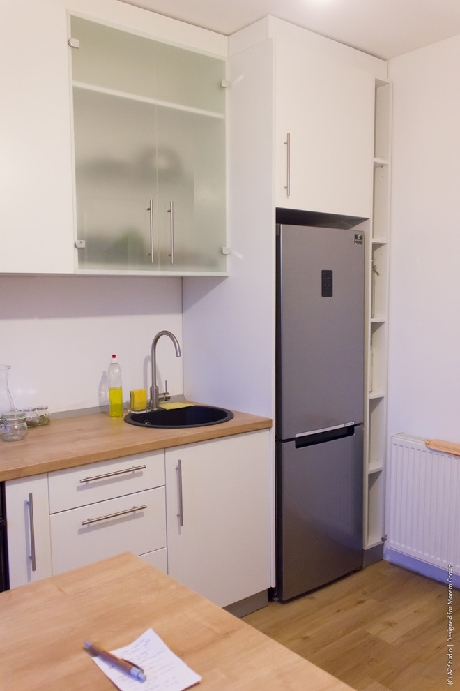 Exempel på ett avskilt, litet modernt linjärt kök, med en enkel diskho, släta luckor, vita skåp, laminatbänkskiva, vitt stänkskydd och plywoodgolv