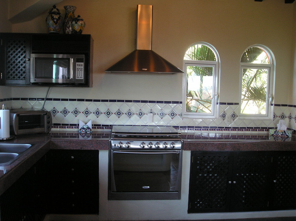 Пример оригинального дизайна: п-образная кухня в средиземноморском стиле с обеденным столом, двойной мойкой, фасадами с филенкой типа жалюзи, темными деревянными фасадами, гранитной столешницей, фартуком из плитки мозаики и техникой из нержавеющей стали