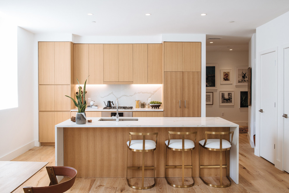 Bild på ett funkis kök, med en integrerad diskho, släta luckor, skåp i mellenmörkt trä, marmorbänkskiva, vitt stänkskydd, stänkskydd i marmor, mellanmörkt trägolv, en köksö och brunt golv
