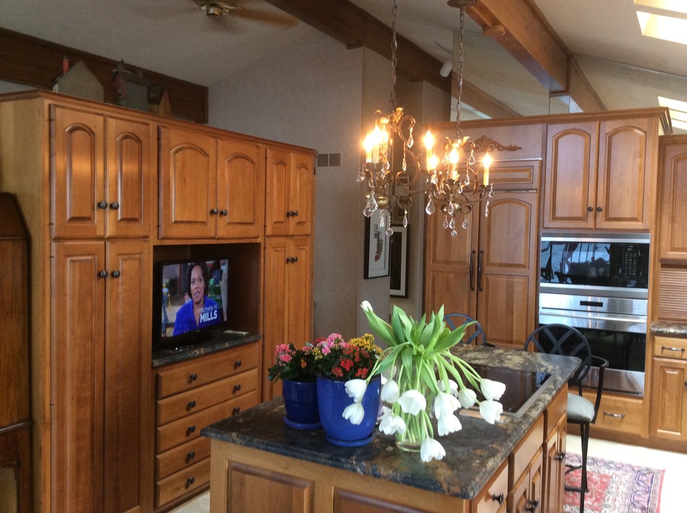 Cette image montre une grande cuisine ouverte traditionnelle en U et bois brun avec un placard avec porte à panneau surélevé, un plan de travail en granite, un électroménager en acier inoxydable et îlot.